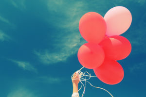 beautiful woman holding red balloons and walking on seaside